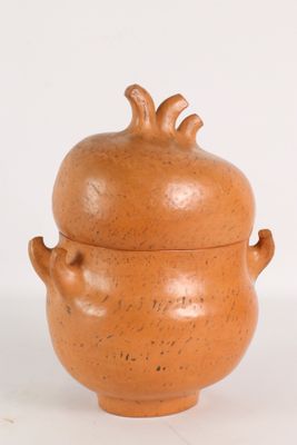 un petit vase marron muni d'un couvercle, posé sur une surface blanche