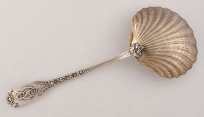 une cuillère en argent ornée d'un coquillage, posée sur un fond blanc
