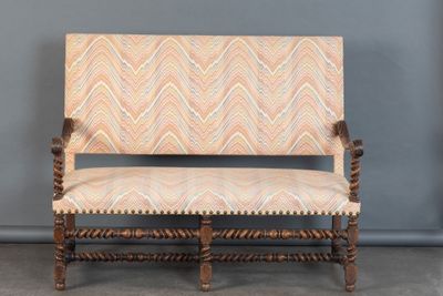 un vieux banc en bois dont l'assise est recouverte d'un tissu à motifs beiges et blancs