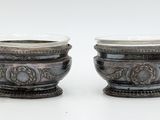two silver vases sitting next to each other on a white surface