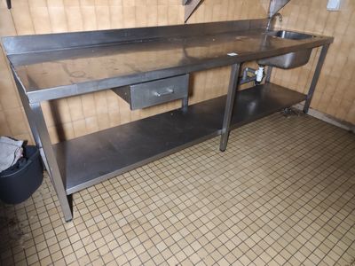 une table en acier inoxydable équipée d'un évier et d'une poubelle