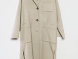 Un manteau beige est suspendu à un cintre devant un mur blanc