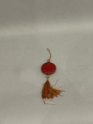 a close up of a red bead with a tassel on a white surface