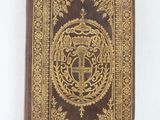 an old book with a gold and black cover on a white surface