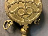 an antique brass plate with a bell hanging from it ' s side