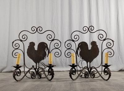 une paire de bougeoirs en fer en forme de coq, sur lesquels sont posées des bougies jaunes