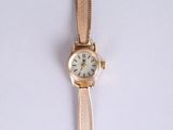 a gold wrist watch with a white face on a white surface