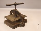 une presse ancienne en fonte avec une poignée en bois, posée sur une surface blanche