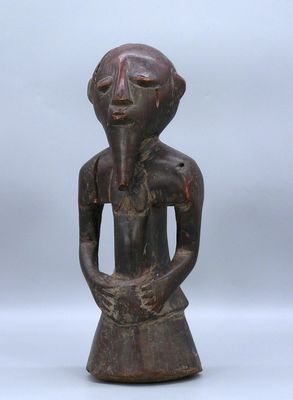 une vieille statue en bois représentant une femme, les mains dans les poches