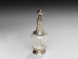 un vase en argent et en verre posé sur un socle, sur une surface blanche