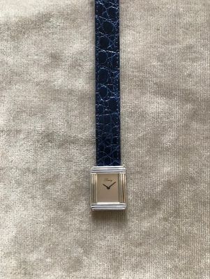 gros plan d'une montre sur une surface blanche avec un bracelet bleu