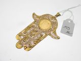 une photo d'un bijou en forme de main de Hamsa en or, sur lequel est apposée une étiquette de prix