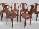 quatre chaises en bois avec des assises recouvertes de cuir et un mur blanc