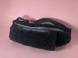 the black purse is on a pink surface with a black strap