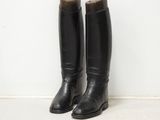 pair of black leather riding boots sitting against a white wall