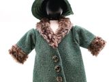 poupée portant un manteau vert et un chapeau muni d'une capuche doublée de fourrure