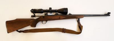 un vieux fusil muni d'une lunette et d'une sangle, posé sur une surface blanche