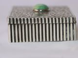 silver box with a green stone on top of it on a white surface