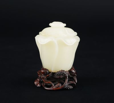 un vase en jade blanc représentant une fleur posée sur un socle, sur fond noir
