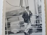 black and white photograph of a man in a suit and hat walking on a deck
