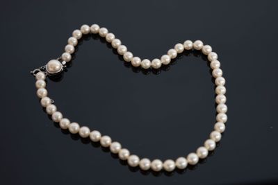 un collier de perles blanches muni d'un fermoir en forme de cœur sur un fond noir