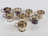 six tasses en métal argenté et une tasse en métal argenté posées sur un fond blanc