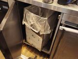 an image of a kitchen with a trash can in the middle of the floor