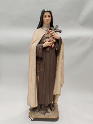 On voit la statue d'une femme tenant une croix, sur fond blanc.