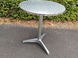 a metal table sitting on top of a sidewalk next to a bush