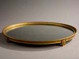 miroir ovale doré posé sur un support blanc, avec un cadre doré