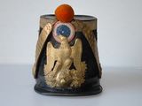 a black and gold vase with an orange on top