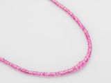 un gros plan d'un collier de perles roses posé sur une surface blanche