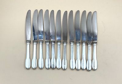 six couteaux argentés sont alignés sur une surface blanche