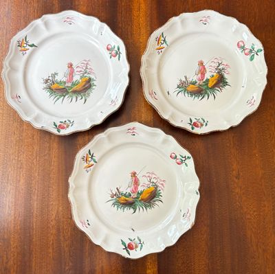 three white plates with birds and flowers on them sitting on a wooden table