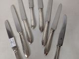 six silver plated knives are arranged in a circle on a white surface