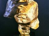 a gold sculpture of a person ' s head with their hands on it