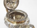 an antique silver plated teapot with a lid on a white surface