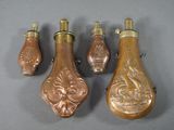 Quatre flacons de parfum en laiton vieilli sont alignés sur une surface grise