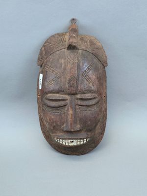 un vieux masque en bois accroché au mur, sur lequel est accrochée une étiquette