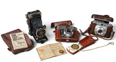 quatre vieux appareils photo et un livre posés sur une surface blanche