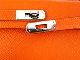 an orange leather bag with a metal handle on a white surface