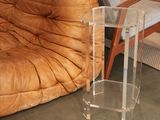 a clear acrylic table on the floor next to a couch