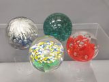 quatre boules de verre de couleurs différentes exposées dans une boîte transparente