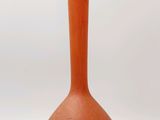 un petit vase orange posé sur une surface blanche
