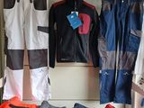 several pairs of pants and jackets hanging on a rack in a room
