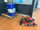 a red lawn mower sitting on the floor next to a blue barrel