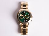 a gold watch with a green face sitting on a white surface