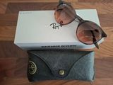 Lunettes de soleil Ray-Ban dans leur boîte et leur étui, posées sur un plancher en bois