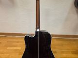 a black acoustic guitar sitting on top of a hard wood floor