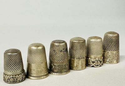 six antique thimbles lined up in a row on a white surface